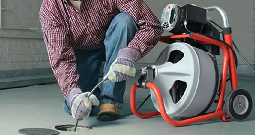 Técnico desentupidor desentupindo esgoto externo com máquina
