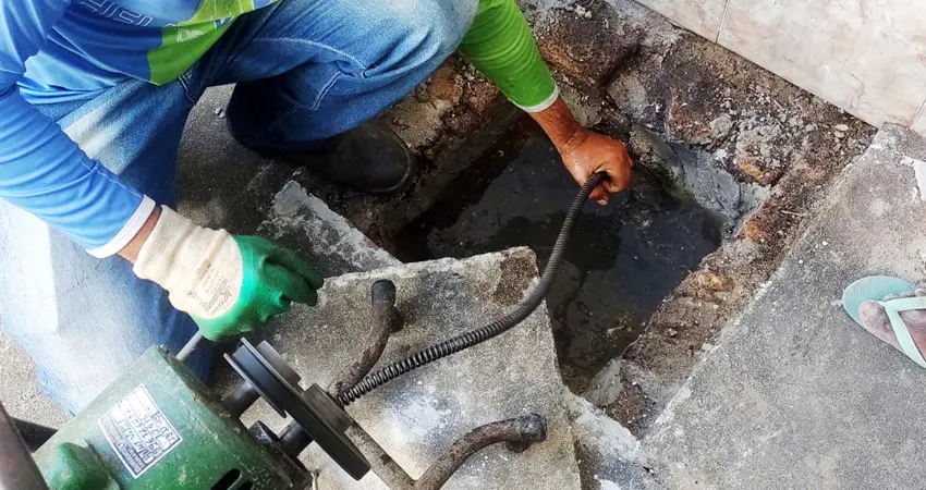 Técnico desentupidor desentupindo esgoto externo com máquina