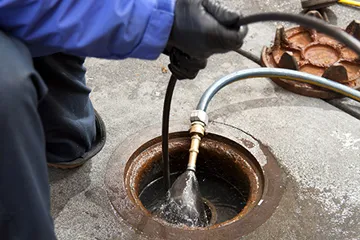Técnico desentupidor desentupindo esgoto externo com máquina de jateamento