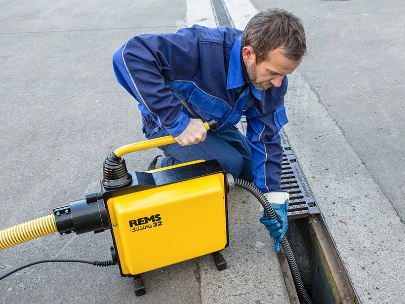 Técnico desentupidor desentupindo esgoto externo com máquina