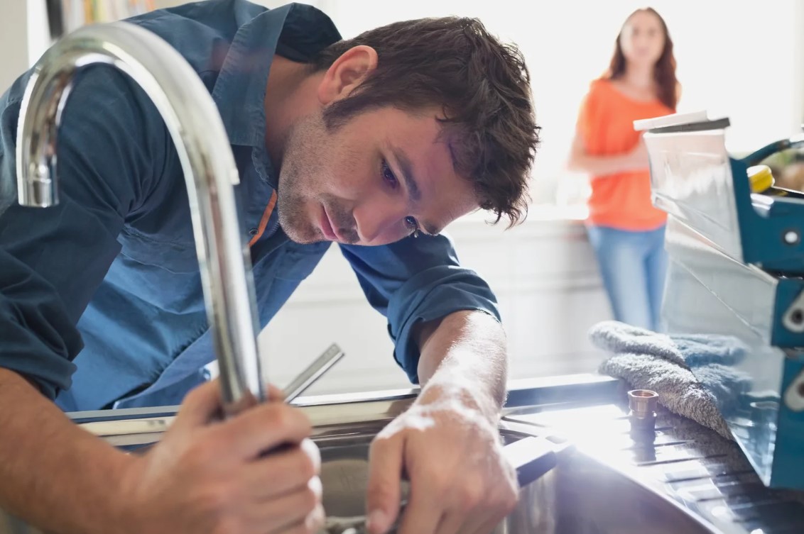 Técnico Encanador consertando torneira de pia e encanamento e cliente observando-o